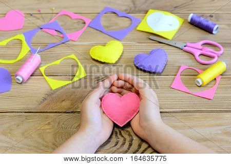 Little girl made a felt heart ornaments. Girl holding a felt heart in his hands. Crafts for Valentine's day or mother's day. Handmade decor. How to create felt valentine ornaments. Easy kids crafts