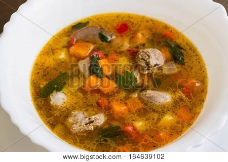 Vegetable soup with chicken giblets in a white bowl on a marble table