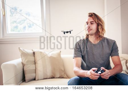 Young man playing with a small quadrocopter drone at home in his living room.