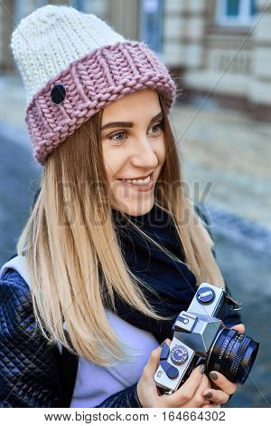 Beautiful girl photographer photographing the old town with retro camera. She is wearing a knitted cap