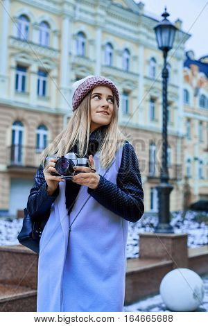 Beautiful girl photographer photographing the old town with retro camera. She is wearing a knitted cap