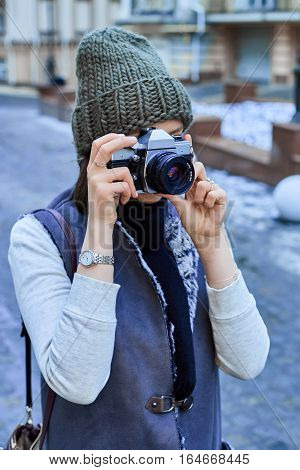 Beautiful girl photographer photographing the old town with retro camera. She is wearing a knitted cap
