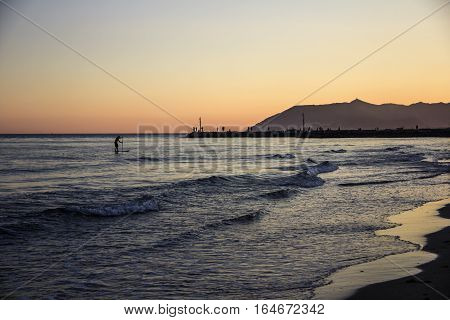 Sunset on Tyrrhenian sea, view of breakwater, SUP surfer, harbor and seacoast of Terracina, Lazio, Italy