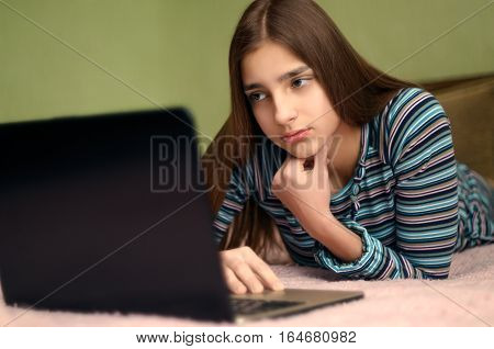 Sad young beautiful girl using laptop computer lying on bed