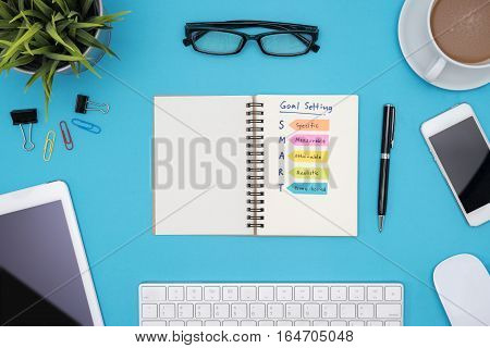 Smart goal setting on notebook with office supplies computer eye glasses and coffee cup over blue desk background Business success concept