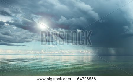 Dramatic sky with large clouds above the lake against black mountains. Lake Baikal.