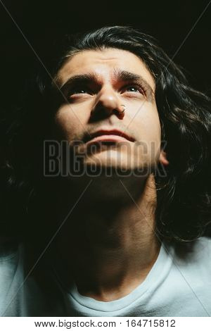 Portrait of a handsome young man with long hair looks up closeup
