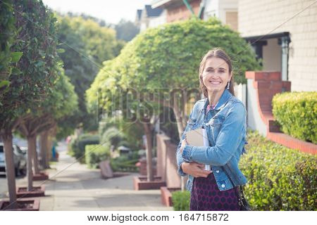 Young attractive woman with books standing in sunny street. She looks successful she is smiling happily she has a whole future ahead of her.