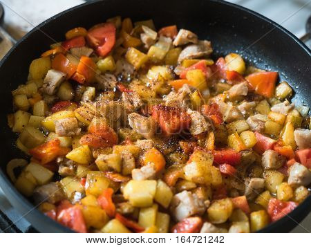 Picture of the frying colourful meal in the frying pan close up. Black frying pan on a white gas stove.