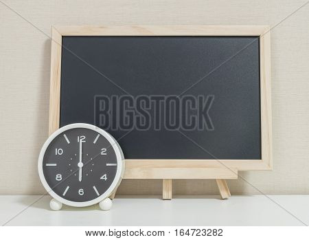 Closeup alarm clock for decorate show 6 o'clock with wood black board on white wood desk and cream wallpaper textured background selective focus at the clock