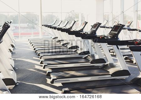 Modern gym interior with equipment. Fitness club with row of treadmills for fitness cardio training in evening backlight. Healthy lifestyle concept