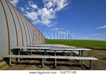 Heavy duty metal picnic tables are stored next to a steel quonset building.