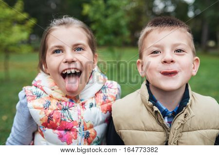 Portrait of a little brother and sister sticking out their tongues and making faces while enjoying a day outside together in autumn