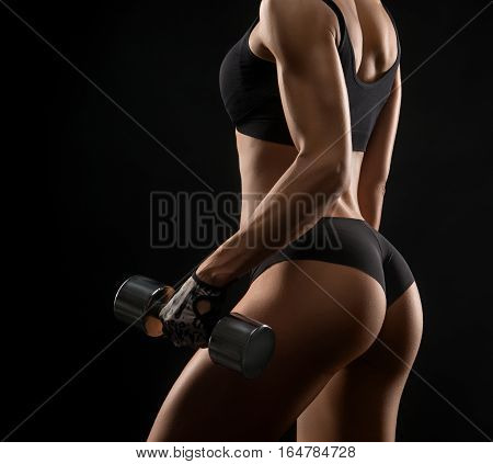Pump your way to fitness. Cropped rearview shot of a fit woman in exercise clothing lifting weights against black background