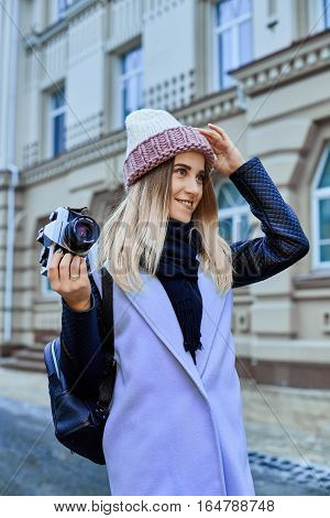 Beautiful girl photographer photographing the old town with retro camera. She is wearing a knitted cap