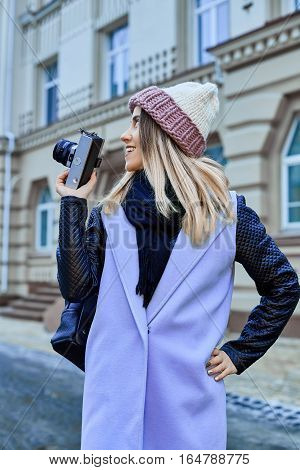 Beautiful girl photographer photographing the old town with retro camera. She is wearing a knitted cap