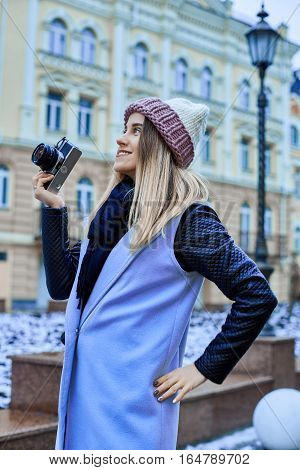 Beautiful girl photographer photographing the old town with retro camera. She is wearing a knitted cap