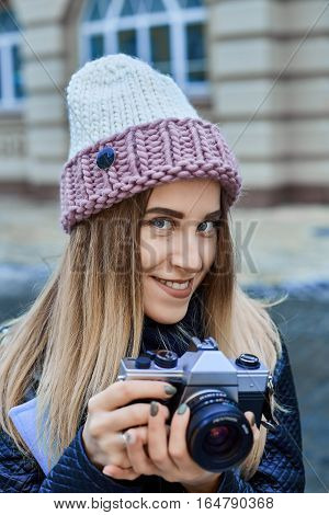 Beautiful girl photographer photographing the old town with retro camera. She is wearing a knitted cap