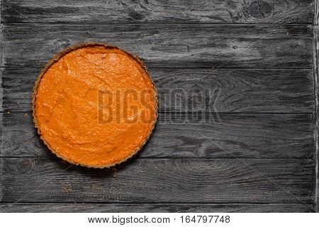 Overhead shot of freshly baked pumpkin pie on background of rustic grey wood planks. Copy space. Homemade pie cooking in fall harvest Thanksgiving autumn. Healthy food.