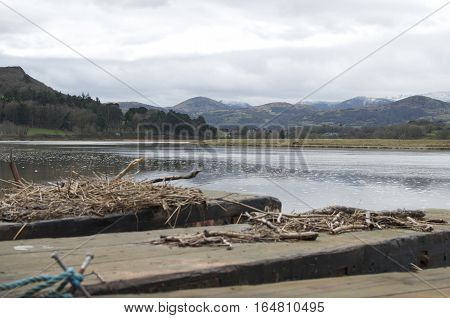 Snowdonia, Snow capped mountains, behind a tranquil river view with wooden jetty with sticks and twigs landscape