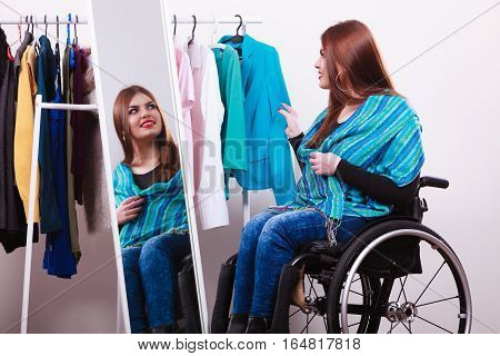 Real people disability and handicap concept. Teen girl handicapped woman sitting on wheelchair choosing clothes in wardrobe or looking for some clothes in shop