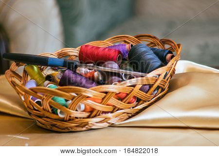 Vintage basket with sewing kit, multi-colored threads on fabric background
