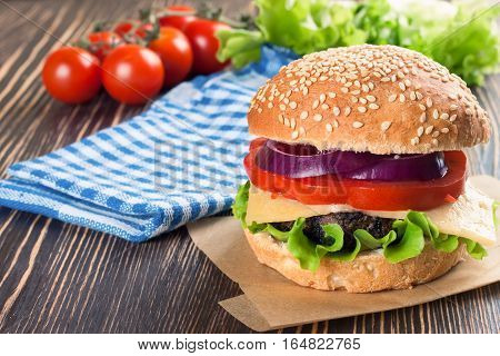 Homemade cheeseburger with beef patties and fresh salad on seasame buns, sered on brown wooden table.