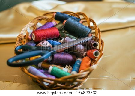 Vintage basket with sewing kit, multi-colored threads on fabric background