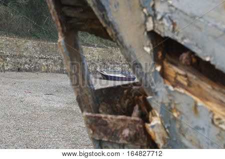 Old wooden rowing boat beached, white and blue framed by wooden wreckage