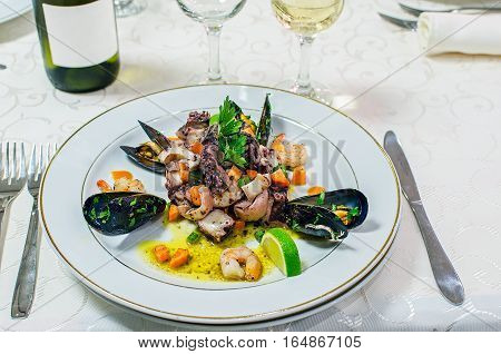 Seafood salad with octopus, shrimp, mussels, scallops, lime and arugula on a white plate.