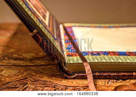 Opened book with the silk laying. Handmade leather cover and bound. Wooden table. Concept for library, reading, education.