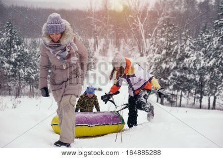 Happy smiling people having fun on snow hill. Two women and child sledding on snow tubings. Winter vacation.