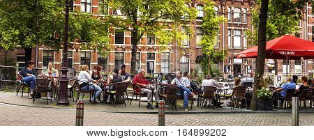 AMSTERDAM NETHERLANDS JULY 9 2016. People is relaxing and have a drink on a terrace along the canal in Amsterdam style of life in Amsterdam Netherlands.