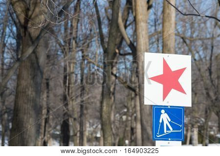 Ski trail sign with picture of skiing and red star to mark the start of path in snowy forest on sunny day for National Ski Day or for cross-country skiing and healthy outdoor winter activities