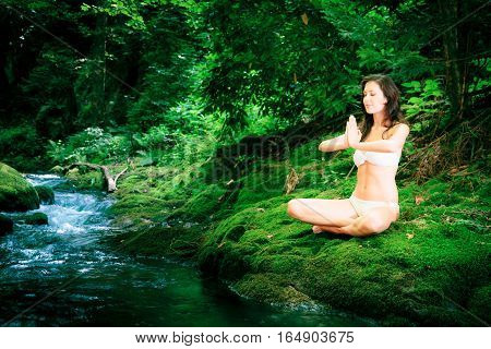 a young beautiful lady is meditating by a river flowing through the forest