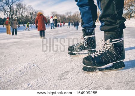 Close-up of ice skating shoes on a rink with people skating in the background (Lafontaine Park Montreal Canada)