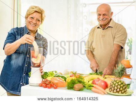 Senior couple preparing vegetarian breakfast with bio organic ingredients at home - Retired people taking care about nutrition and diet - Healthy lifestyle concept - Focus on man face - Warm filter