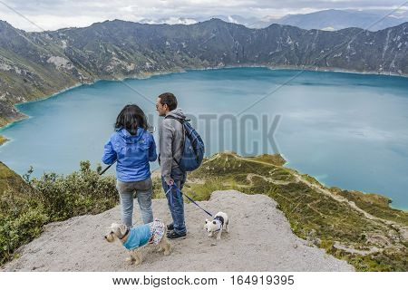 QUILOTOA, ECUADOR, FEBRAURY - 2016 - Couple with two dogs watching the view at Quilotoa lake Ecuador