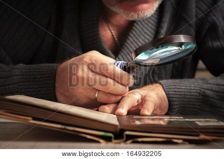 Man considers album of stamps trough the magnifying glass horizontal