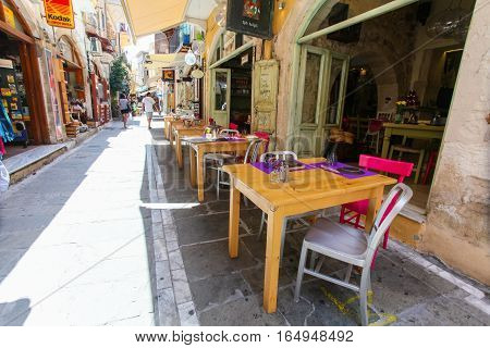 Rethymnon, Island Crete, Greece - June 23, 2016: Tables and chairs of cafe are on the narrow street of Rethymnon (part of Old Town)