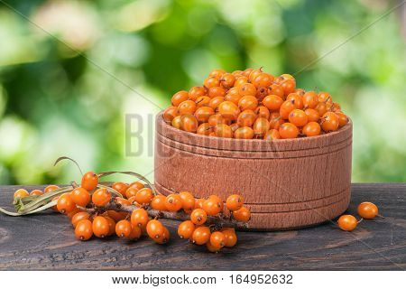 Sea-buckthorn berries in a wooden bowl on a table with blurred garden background.