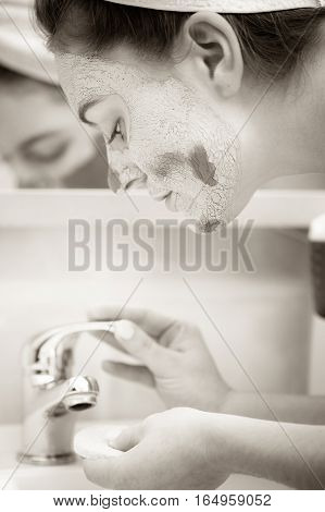 Woman Removing Facial Clay Mud Mask In Bathroom