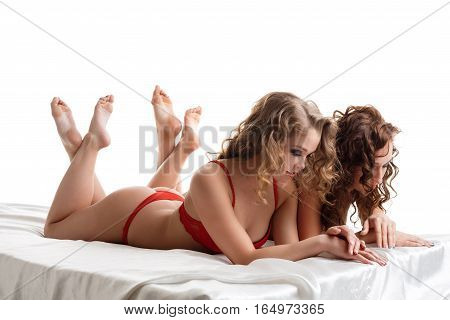 Long haired curly young blonde and brunette lying in bed on stomacks in sexy lingerie studio shot