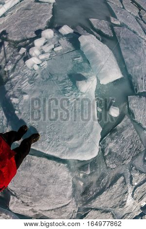top view of a human foot on the ice is covered with cracks and hummocks.