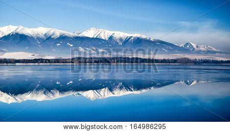 Rreflection on lake Liptovska Mara Slovakia covered in ice.on a quiet winter days. Backround of West an High Tatras mountains Slovakia. Beautiful landscape