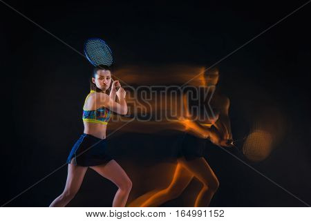 Portrait of beautiful girl tennis player with a racket on dark studio background. Stroboscope shooting technique