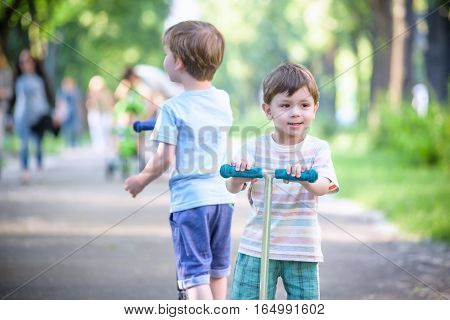 Two Cute Boys, Compete In Riding Scooters, Outdoor In The Park, Summertime.