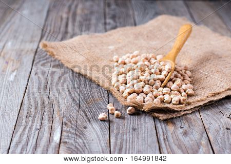 Dry and uncooked chickpeas in spoon on wooden background