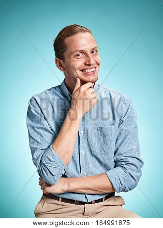 Happy excite young man in blue shirt smiling and celebrating his succcess over blue studio background