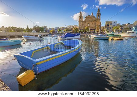 Msida Malta - Blue traditional fishing boat with the famous Msida Parish Church at background on a summer day with blue sky and clouds